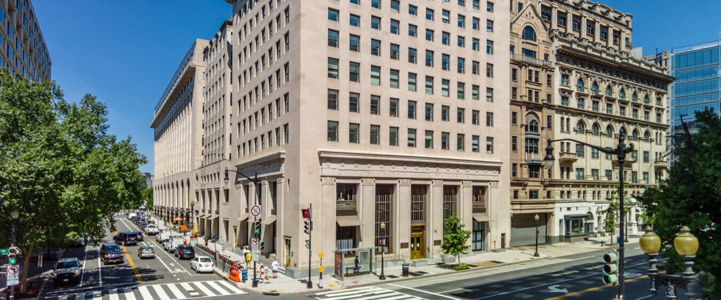 Corner view of 700 14th Street NW in Washington DC showing historic stone façade and busy street activity.